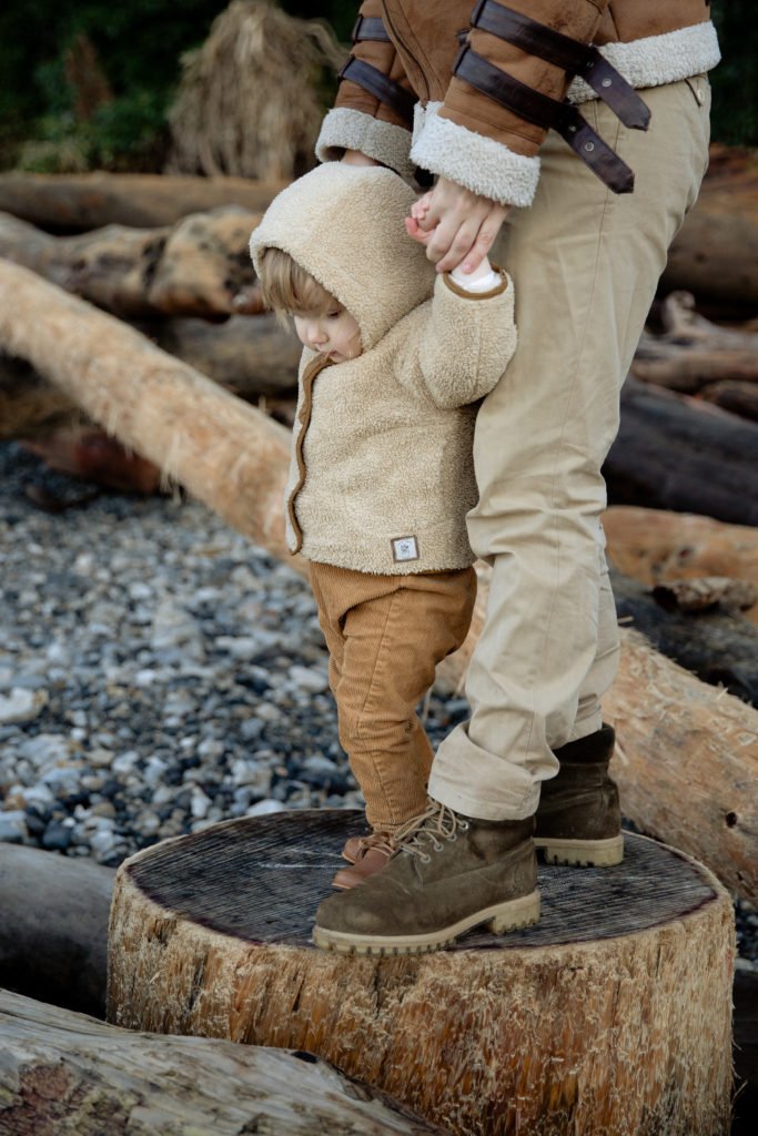 crop person standing adorable kid on wooden logs in seashore 3932886